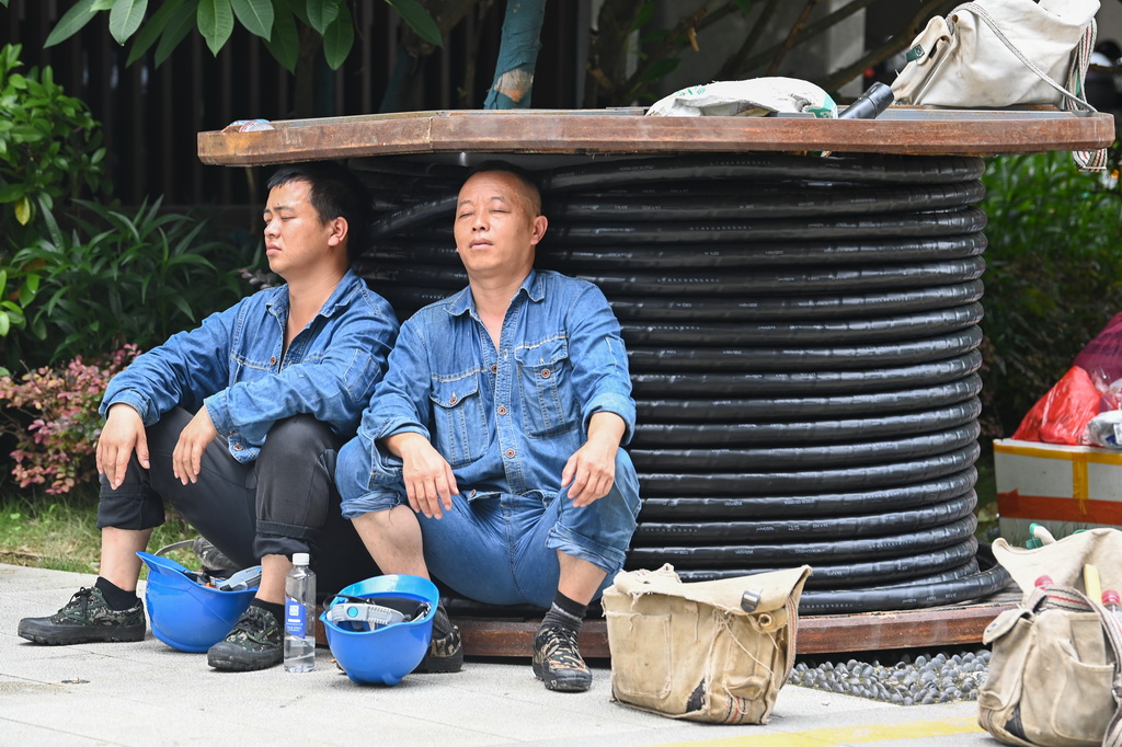 7月10日，在广西贵港市，两名从贵州前来支援的电力抢修工人在工作间隙靠着电缆休息。新华社记者 曹祎铭 摄