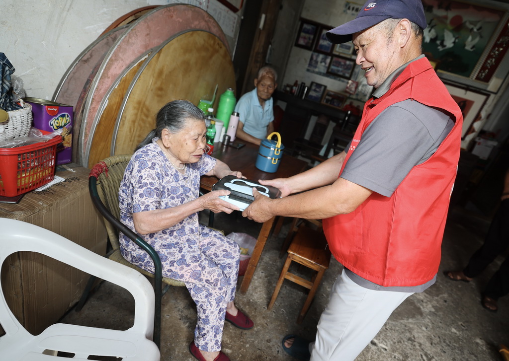 7月28日，荻浦村老年食堂的志愿者申屠名升（右）给村里96岁高龄老人邓国香送餐。