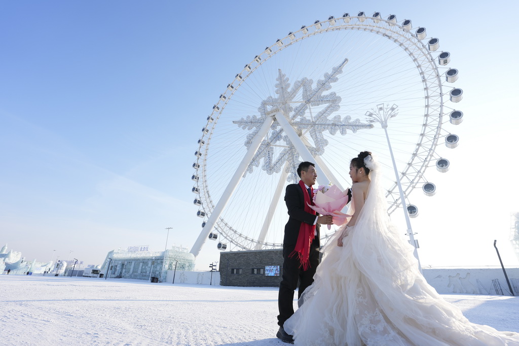 在哈尔滨冰雪大世界举行的哈尔滨第四十二届“四季沐歌”公益冰雪集体婚礼上，一对新人在摩天轮下拍照留念（1月6日摄）。新华社记者 王松 摄