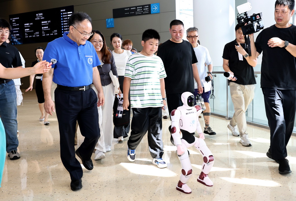 8月18日，来自山东省滨州市的张志恒小朋友（中）和爸爸妈妈一起，在上海科技馆馆长倪闽景（前左一）陪同下，由机器人引导走进活动现场。