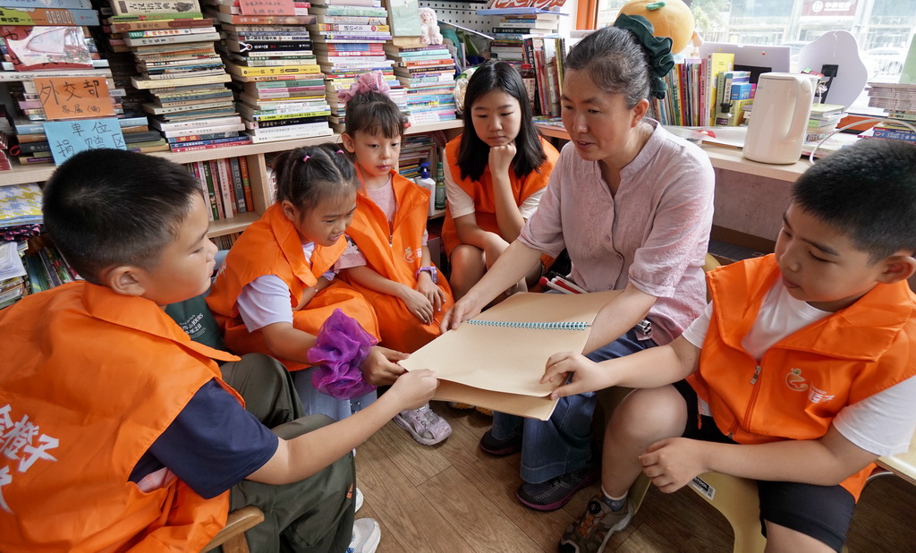 8月25日，视障志愿者曾鑫（右二）在金橙子众享驿站内为小志愿者们分享盲文图书知识。