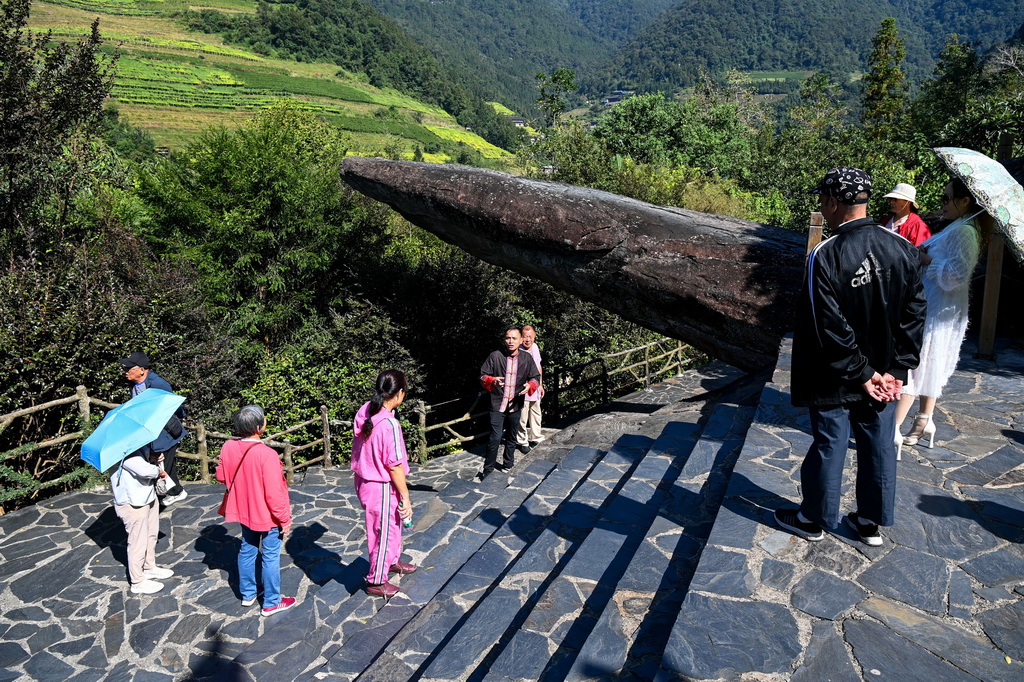 10月9日，在龙胜各族自治县周家村白面瑶寨，秦新发（中）为游客讲解“红军岩”的故事。