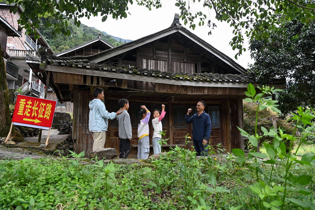 10月5日，在龙胜各族自治县周家村白面瑶寨，秦新发（右一）给小朋友讲述红军长征的故事。
