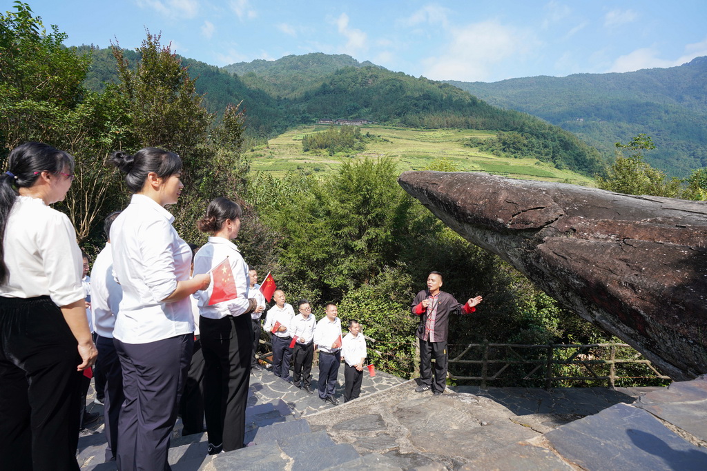 9月30日，在龙胜各族自治县周家村白面瑶寨，秦新发（右一）为参观者讲解“红军岩”的故事。