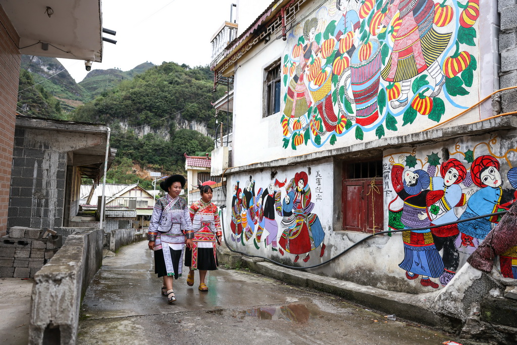 贵州省六盘水市水城区陡箐镇陡箐村的画师罗班妹（左）与女儿从村里的农民画前经过（10月5日摄）。